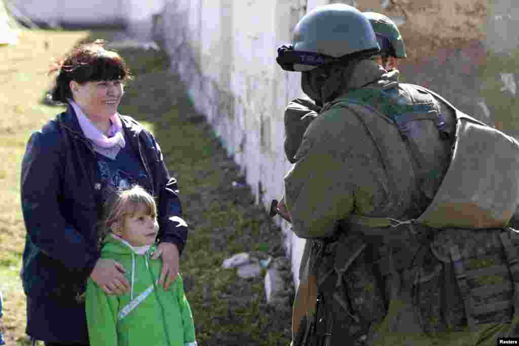 Seorang gadis cilik Ukraina memandang seorang tentara, yang diyakini merupakan anggota pasukan Rusia, yang berdiri di luar unit militer Ukraina di desa Perevalnoye, di luar kota Simferopol, Ukraina (3/3). (Reuters/Baz Ratner)