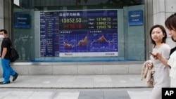 People walk by an electronic stock board of a securities firm in Tokyo Monday, July 1, 2013. Global stocks swung between gains and losses Monday after China's manufacturing weakened in June amid a credit crunch. Tokyo's Nikkei 225 rose 1.3 percent to 13,8