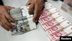 A clerk counts Chinese yuan and U.S. dollar banknotes at a branch of Bank of China in Taiyuan, China, Jan. 4, 2016.