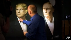 A journalist points at a portrait of U.S. President-elect Donald Trump, with a portrait of Russian President Vladimir Putin at right, during a live telecast of the U.S. presidential election in the Union Jack pub in Moscow, Russia, Nov. 9, 2016. 