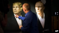 A journalist points at a portrait of U.S. President-elect Donald Trump, with a portrait of Russian President Vladimir Putin at right, during a live telecast of the U.S. presidential election in the Union Jack pub in Moscow, Russia, Nov. 9, 2016. 