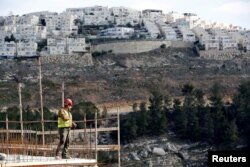 A laborer works at a construction site in the Israeli settlement of Ramot, as the Israeli settlement of Ramat Shlomo is seen in the background, in an area of the occupied West Bank that Israel annexed to Jerusalem, Jan. 22, 2017.