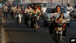 A local woman, foreground right, drives her motorbike as she carries her baby and a dog on a busy street in Phnom Penh, Cambodia, Tuesday, Feb. 18, 2014. (AP Photo/Heng Sinith)