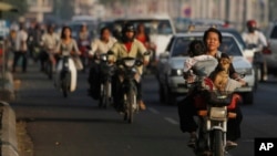 A local woman, foreground right, drives her motorbike as she carries her baby and a dog on a busy street in Phnom Penh, Cambodia, Tuesday, Feb. 18, 2014. (AP Photo/Heng Sinith)