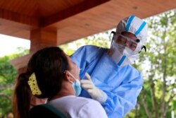 A medical worker in protective suit collects a swab sample from a woman for nucleic acid testing following two imported coronavirus disease (COVID-19) infections from neighbouring Myanmar, at a hotel in the border city of Ruili, Dehong prefecture, Yunnan