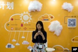 FILE - A woman uses her smartphone near a booth promoting cloud services during the Global Mobile Internet Conference in Beijing, China.