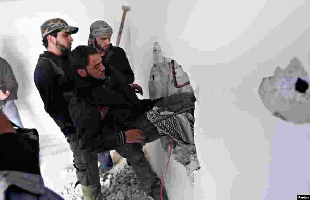 Fighters from the Free Syrian Army&#39;s Tahrir al Sham brigade carry a wounded fighter through a hole in a wall during heavy fighting in the Mleha suburb of Damascus, January 26, 2013.