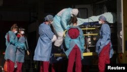 COVID-19 ရောဂါ အကြီးအကျယ်ကူးစက်နေတဲ့ လန်ဒန်မြို့မှာရှိနေတဲ့ St Thomas' ဆေးရုံမှာ အရေးပေါ်လူနာ တင်ယာဉ်က လူနာ တဦးကို သယ်ယူနေတဲ့ ကာကွယ်ရေးဝတ်စုံ ဝတ်ဆင်ထားတဲ့ ကျန်းမာရေးဝန်ထမ်းများ
