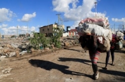 People carry their belongings as they evacuate during riots over the demolition of homes at the Mukuru Kwa Njenga informal settlements in Nairobi, Dec. 27, 2021.