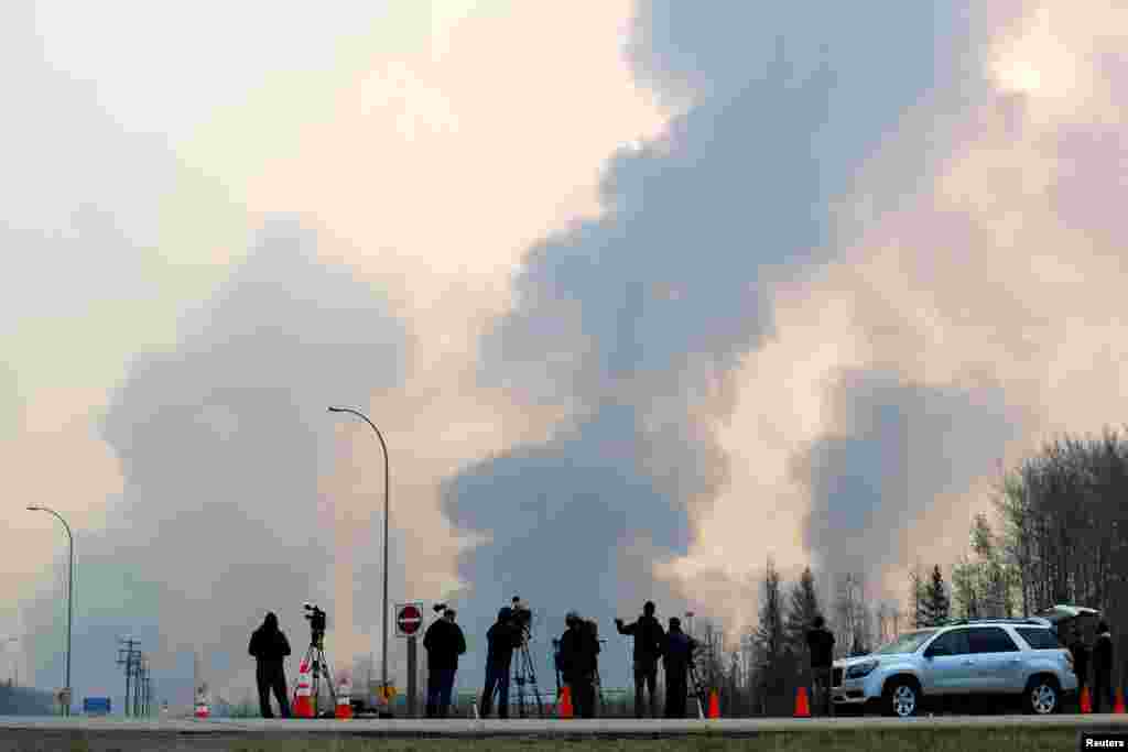 Para wartawan memperhatikan asap hitam yang mengepul dari kebakaran hutan di selatan Fort McMurray, Alberta, Kanada.