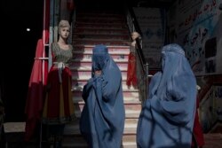 Dua perempuan Afghanistan yang mengenakan burqa melintas di depan toko pakaian di Kabul, November 2021. (Foto: Associated Press)