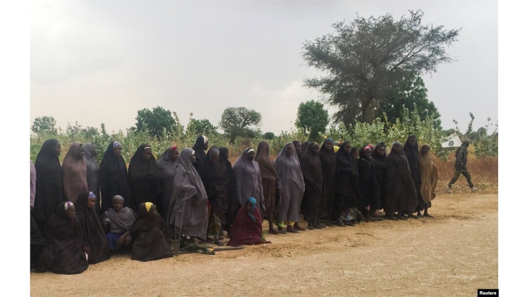 A man carrying a Boko Haram flag walks past a group of 82 Chibok girls, who were held captive for three years by Islamist militants, as the girls wait to be released in exchange for several militant commanders, near Kumshe, Nigeria, May 6, 2017.