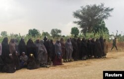 A man carrying a Boko Haram flag walks past a group of 82 Chibok girls, who were held captive for three years by Islamist militants, as the girls wait to be released in exchange for several militant commanders, near Kumshe, Nigeria, May 6, 2017.