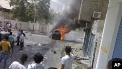 By-standers watch as a booby-trapped car burns after an explosion in the southern Yemeni port city of Aden, July 20, 2011