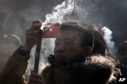 FILE - A Chinese man uses iPhone to take picture as he prays for health and fortune on the first day of the New Year at Yonghegong Lama Temple in Beijing, Jan. 1, 2019.