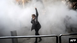 An Iranian woman raises her fist amid the smoke of tear gas at the University of Tehran during a protest, in Tehran, Dec. 30, 2017. The Iranian government said, Jan. 14, 2017, that 25 people had been killed during recent anti-government protests.