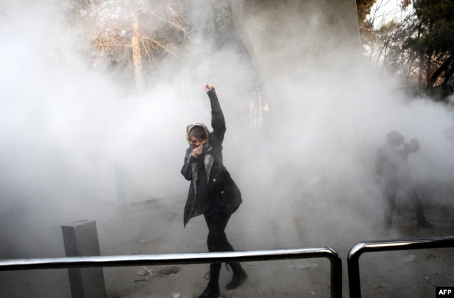 FILE - An Iranian woman raises her fist amid the smoke of tear gas at the University of Tehran during a protest, in Tehran, Iran, Dec. 30, 2017.