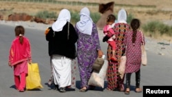 FILE - Women and children from the minority Yazidi sect, fleeing the violence in the Iraqi town of Sinjar, walk to a refugee camp after they re-entered Iraq from Syria at the Iraqi-Syrian border crossing in Fishkhabour, Dohuk province, Aug. 14, 2014.