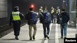 A police officer escorts migrants from a train at Hyllie station outside Malmo, Sweden, Nov. 19, 2015.