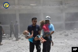 This photo provided by the Syrian Civil Defense group known as the White Helmets, shows civil defense workers carrying children after airstrikes hit a school housing a number of displaced people, in the western part of the southern Daraa, Syria, June 14, 2017.