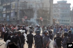 Ethnic Madhesi protesters stand near smoke from a tire set on fire by them, as Nepalese policemen stand guard near the Central Development Office at Birgunj, a town on the border with India, Nepal, Nov. 2, 2015.