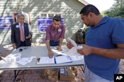 In this Sept. 23, 2016, photo, Mohammad Ali Chaudry, left, president of the Islamic Society of Basking Ridge, New Jersey, and Shawn Butt provide voter registration information to Shahul Feroze, right, after a prayer service.