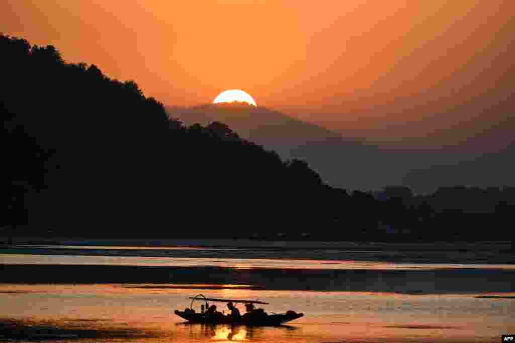 Fisherman sit on a small boat at Dal Lake during sunset in Srinagar, India.