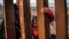  FILE - A migrant climbs the border fence before jumping into the U.S. in San Diego, California, from Tijuana, Mexico, Dec. 27, 2018. 