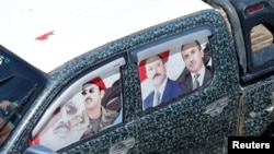FILE - A vehicle with posters of Yemen's former president Ali Abdullah Saleh and his eldest son, Ahmed, on its window glass drives in floodwater during a rainy day in the old quarter of Sanaa, Yemen, Aug. 9, 2017.