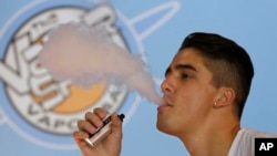 FILE - A smoker exhales vapor from an e-cigarette at the Vapor Spot, in Sacramento, California, in this July 7, 2015, photo. On Thursday, the U.S. government announced a ban on the sale of e-cigarettes, pipe tobacco, hookah tobacco and cigars to minors.