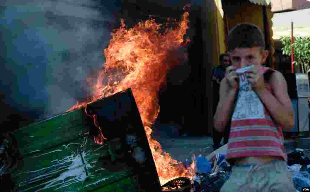 A young boy covers his face near a burning dumpster in the Bab Tabbaneh neighborhood of Tripoli, Lebanon, August 25, 2012. (VOA/Jeff Neumann)