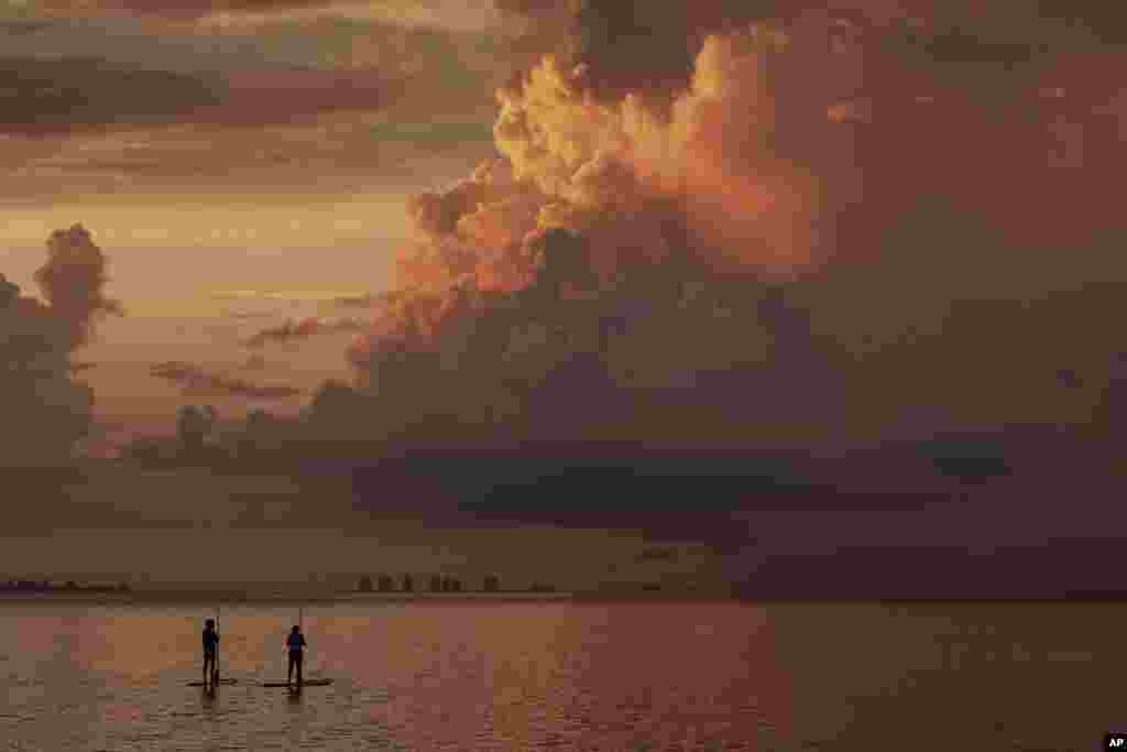 Two paddle boarders watch as the sun rises during a stormy morning in Sanibel, Florida.