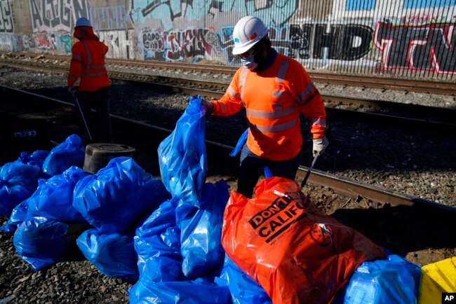 Para petugas membersihkan kardus-kardus dan barang-barang bekas lainnya di lokasi rel kereta api Union Pacific, Los Angeles, 20 Januari 2022. (AP)