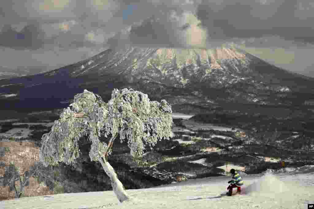 A man snowboards down a slope overlooking Mount Yotei at a ski resort in Niseko, Hokkaido, Japan.