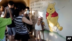 A child poses for photos near a mural depicting Winnie the Pooh in Shanghai, China, Aug. 8, 2018. 