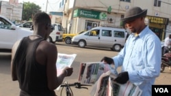 A man buys a newspaper from a street vendor in Westfield, Banjul, Gambia, June 7, 2017. (S.Christensen/VOA)