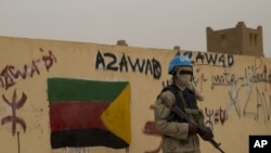 FILE - A United Nations peacekeeper stands guard at the entrance to a polling station covered in separatist flags and graffiti supporting the creation of the independent state of Azawad, in Kidal, Mali, July 28, 2013. 