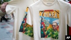 FILE - People examine T-shirts depicting Russian President Vladimir Putin and reading Greetings from Crimea at the biggest department store GUM in Moscow's Red Square.