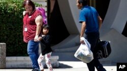 A child holds the hand of a Lutheran Social Services worker as they arrive at Lutheran Social Services, July 26, 2018, in Phoenix. Lutheran Social Services officials stated they were expecting reunited families separated at the border when apprehended entering the United States to come through their facility.