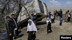 FILE - Schoolgirls walk past a damaged minibus after it was hit by a bomb blast in the Bagrami district of Kabul, Afghanistan.