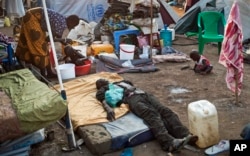 A sick displaced man lies asleep on a bed while a mother bathes her son and keeps an eye on her other child in the United Nations camp in Juba, South Sudan, Feb. 12, 2014.