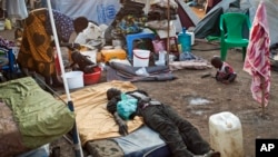 A sick displaced man lies asleep on a bed while a mother bathes her son and keeps an eye on her other child in the United Nations camp in Juba, South Sudan, Feb. 12, 2014.