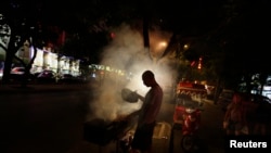 FILE - A man fans a grill while cooking kebabs at a roadside stall, in central Beijing.