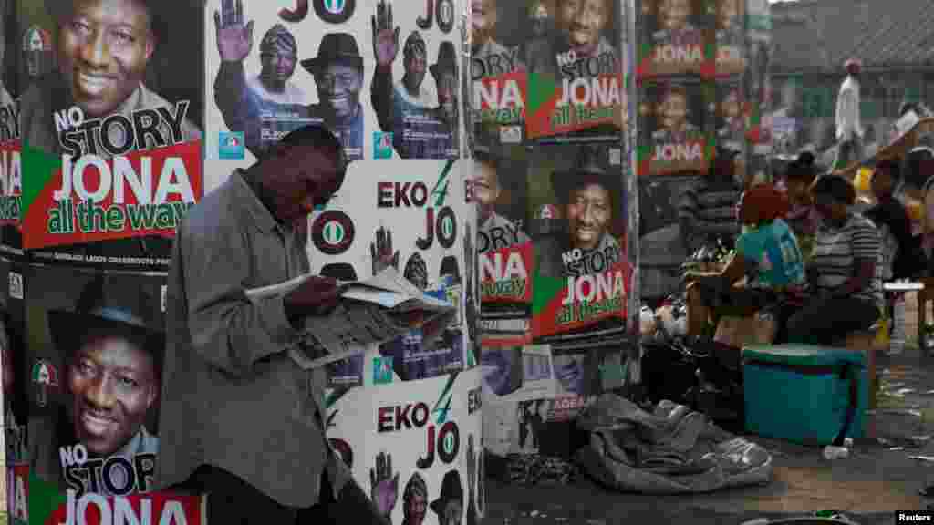 Homem lendo um Jornal na frente de pôsteres da campanha eleitoral em Lagos.