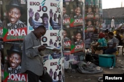 A man reads a newspaper in front of electoral campaign posters in Lagos, Nigeria, March 30, 2015.