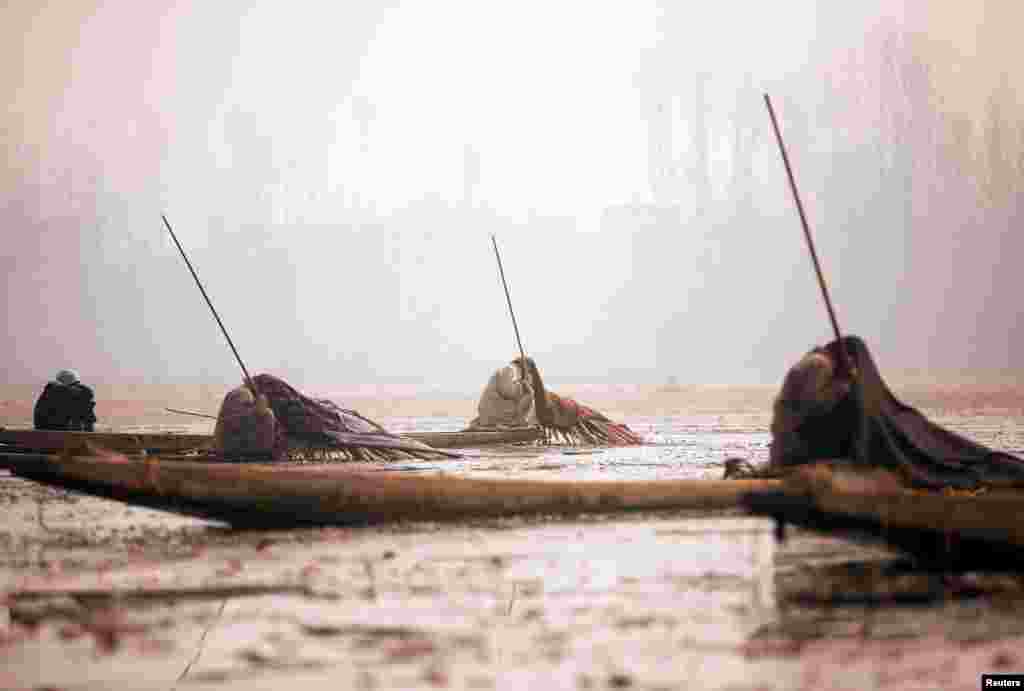 Para nelayan Kashmir menyelimuti tubuh dan kepala mereka dengan selimut, saat memancing di Danau Anchar pada hari yang dingin membeku di Srinagar, Kashmir-India.