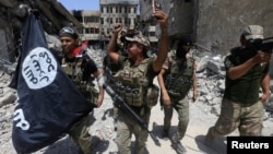 FILE - Members of Iraq's Emergency Response Division hold an Islamic State flag that they pulled down as they celebrate in the Old City of Mosul, Iraq, July 8, 2017. Islamic State fighters have mostly been pushed out of Iraq and Syria but are far from defeated.