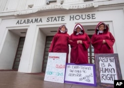 Bianca Cameron-Schwiesow, from left, Kari Crowe and Margeaux Hartline, dressed as handmaids, take part in a protest against HB314, the abortion ban bill, at the Alabama State House in Montgomery, Ala., April 17, 2019.