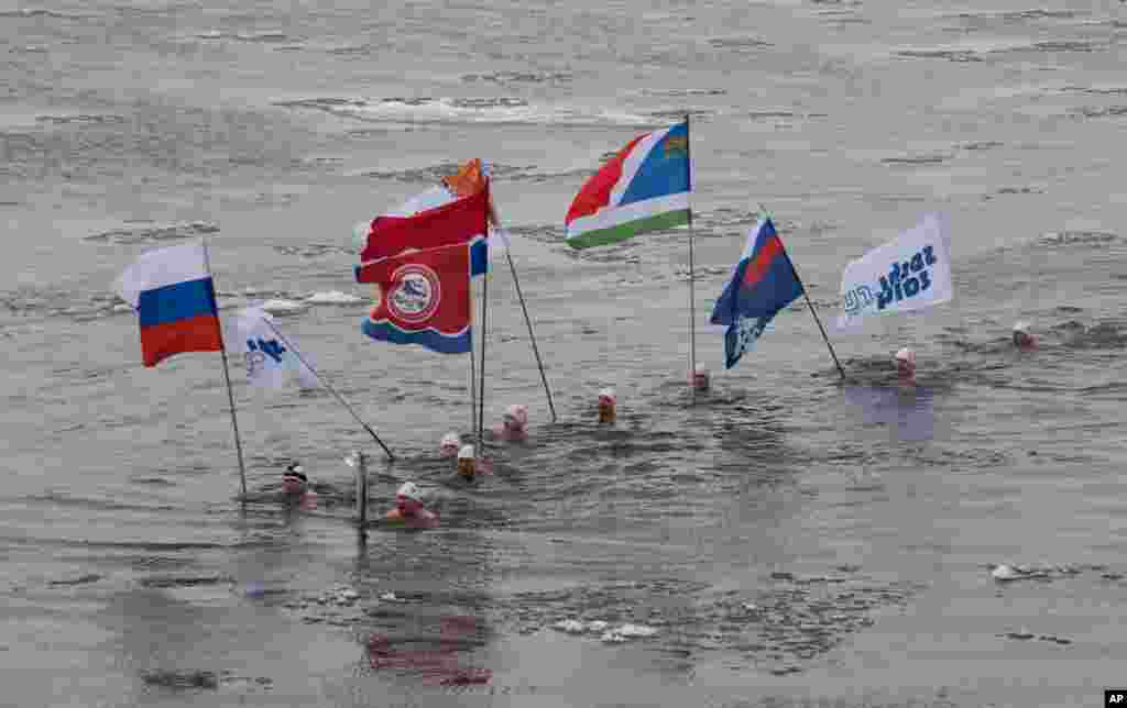 In this photo provided by Olympictorch2014.com torch bearer Alexander Brylin, with other ice swimmers, swims with Olympic torch during the torch relay in the Amur River in Blagoveshchensk, Russia&#39;s Far East.