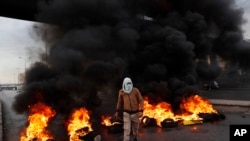 FILE - A protester passes burning tires along a main highway that leads to Beirut's international airport during a protest against the increasing prices of consumer goods and the crash of the local currency in Beirut, Nov. 29, 2021.